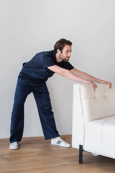 Worker in uniform moving white sofa in apartment — Stock Photo