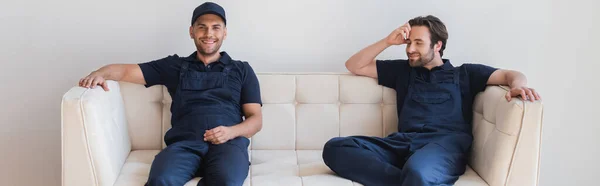 Positive Handwerker in Overalls sitzen auf weißer Couch, Banner — Stockfoto