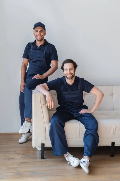 Contremaîtres heureux souriant à la caméra sur le canapé blanc dans le salon — Photo de stock