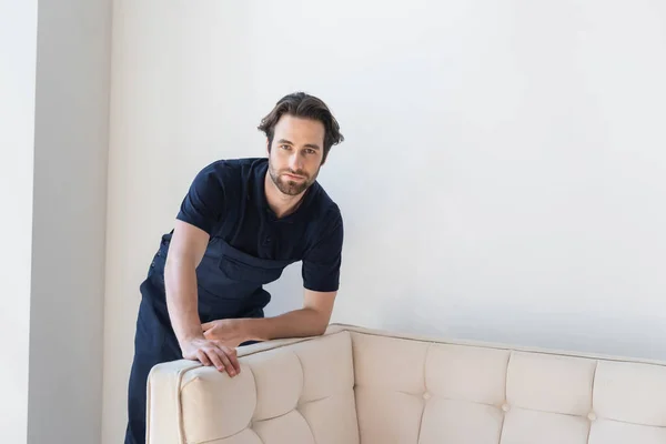 Young foreman in uniform looking at camera near white couch — Stock Photo