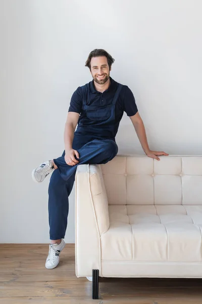 Contremaître en uniforme et baskets souriant à la caméra sur canapé blanc — Photo de stock