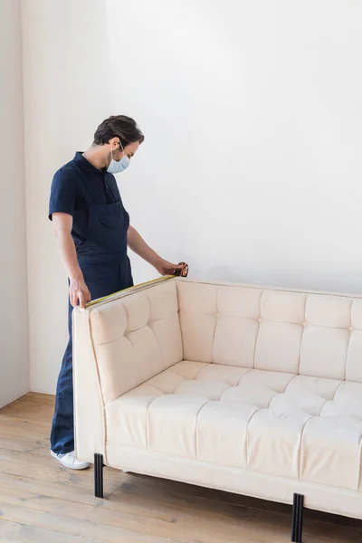 Déménageur en salopette mesurant canapé blanc dans un appartement moderne — Photo de stock