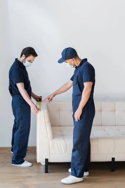 Workman in safety mask pointing near colleague measuring white couch — Stock Photo