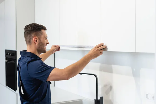 Happy handyman measuring modern furniture in kitchen — Stock Photo