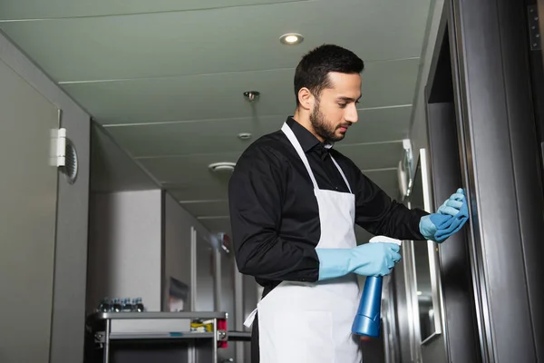 Bearded housekeeper in rubber gloves cleaning corridor in hotel — Stock Photo