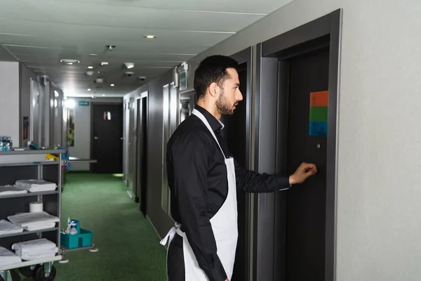 Seitenansicht der bärtigen Haushälterin, die im Hotelzimmer an die Tür klopft — Stockfoto