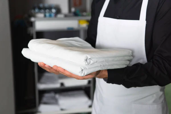 Cropped view of housekeeper holding white clean bed sheets — Stock Photo
