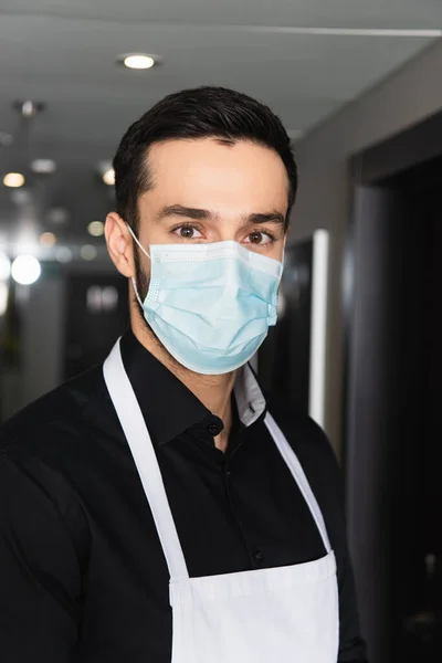 Housekeeper in medical mask looking at camera in corridor of hotel — Stock Photo