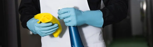 Vista parcial de la ama de llaves en guantes de goma sosteniendo botella de spray con trapo, pancarta - foto de stock