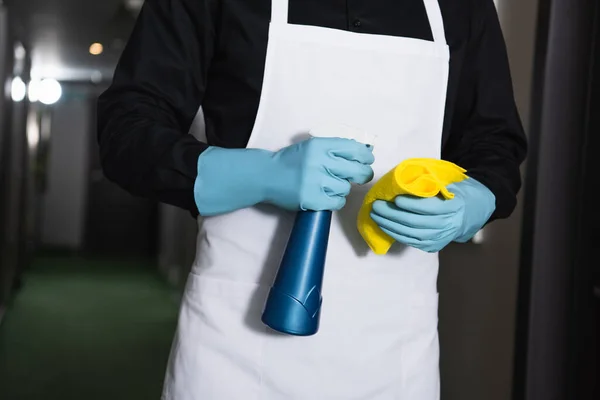 Partial view of housekeeper in rubber gloves holding spray bottle with rag — Stock Photo