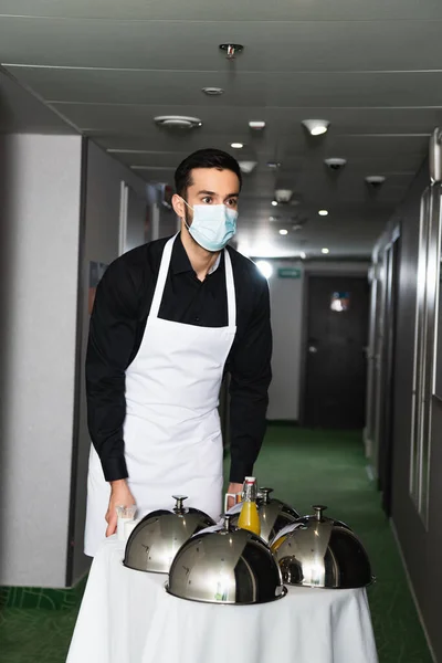 Cameriere in maschera medica e grembiule consegna vassoio con cloche e succo d'arancia — Foto stock