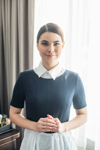 Empregada feliz em uniforme sorrindo no quarto — Fotografia de Stock