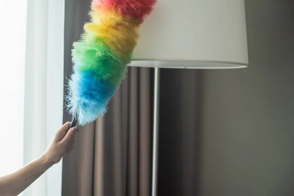 Cropped view of maid cleaning floor lamp with dust brush in hotel room — Stock Photo