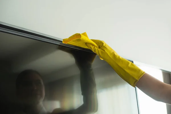 Cropped view of housekeeper in rubber glove cleaning tv display with rag — Stock Photo