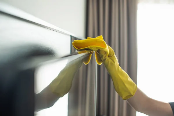 Partial view of housekeeper in rubber glove cleaning tv display with rag — Stock Photo