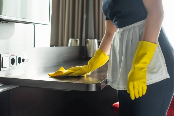 Partial view of housekeeper in rubber gloves cleaning wooden surface with rag — Stock Photo