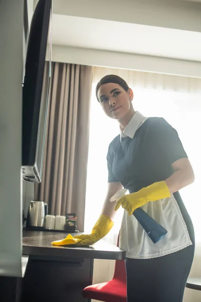 Joven criada en guantes de goma limpiando superficie de madera con trapo - foto de stock