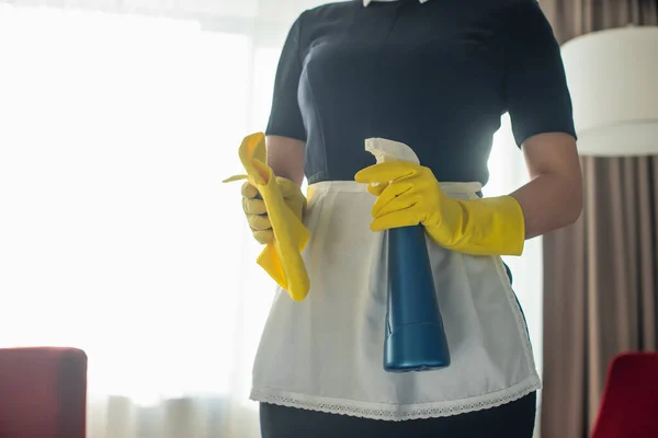 Vista parcial de la joven criada en guantes de goma sosteniendo botella de spray y trapo - foto de stock