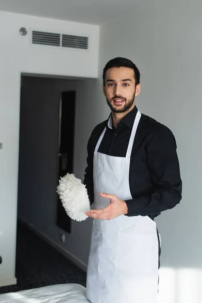 Governante barbuto in grembiule tenendo spazzola di polvere sulla camera d'albergo — Foto stock