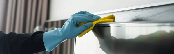 Partial view of housekeeper in blue rubber glove cleaning tv display with rag, banner — Stock Photo