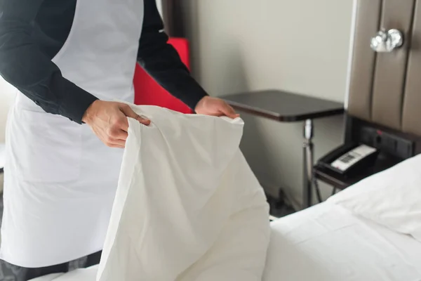 Partial view of housekeeper in apron changing bedding in hotel room — Stock Photo