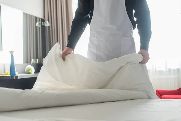 Vista recortada de ama de llaves cambiando ropa de cama blanca en la habitación de hotel - foto de stock