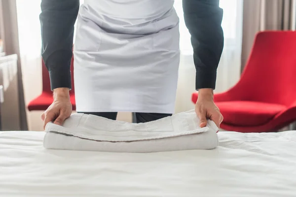 Abgeschnittene Ansicht der Haushälterin, die frische Handtücher auf das Bett im Hotelzimmer legt — Stockfoto