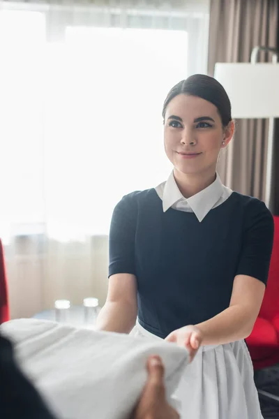 Gaie femme de chambre donnant des serviettes à un collègue flou — Photo de stock