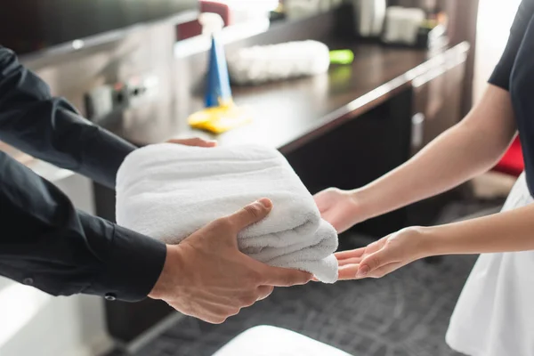 Vista recortada de ama de llaves dando toallas blancas limpias a la criada en la habitación de hotel - foto de stock