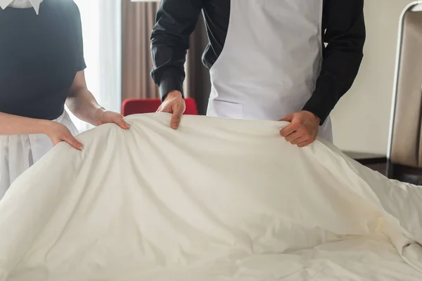 Vista recortada de las amas de llaves cambiando ropa de cama en la habitación de hotel - foto de stock