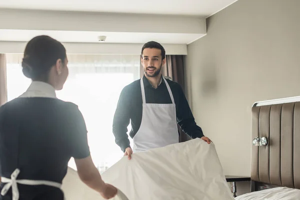 Ama de llaves feliz cambio de ropa de cama en la habitación de hotel - foto de stock