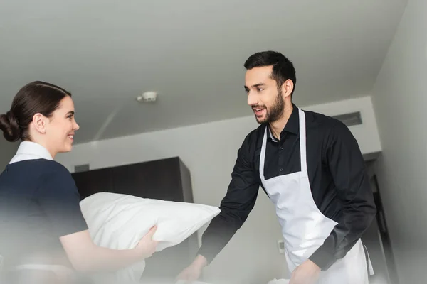 Jovens donas de casa positivas mudando de roupa de cama no quarto de hotel moderno — Fotografia de Stock