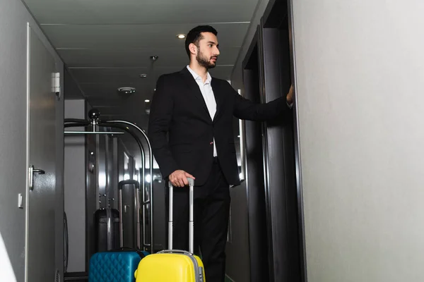 Mann im Anzug steht in der Nähe von Gepäck und klopft an Tür in Hotel — Stockfoto