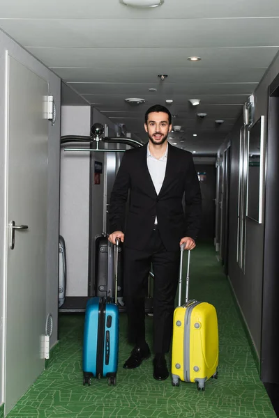 Hombre alegre caminando con equipaje en el pasillo del hotel - foto de stock