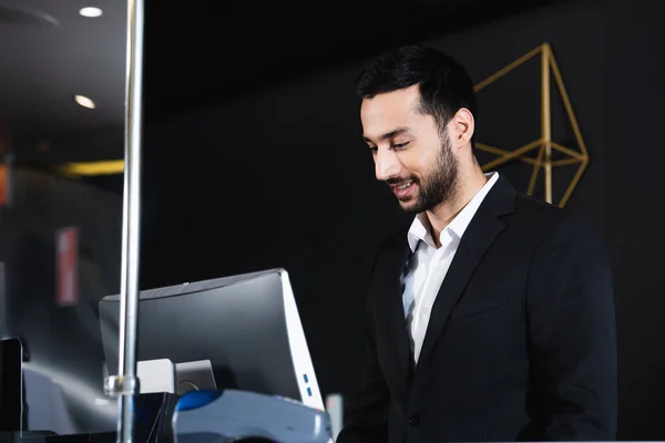 Recepcionista sorrindo trabalhando perto do monitor do computador no hotel — Fotografia de Stock