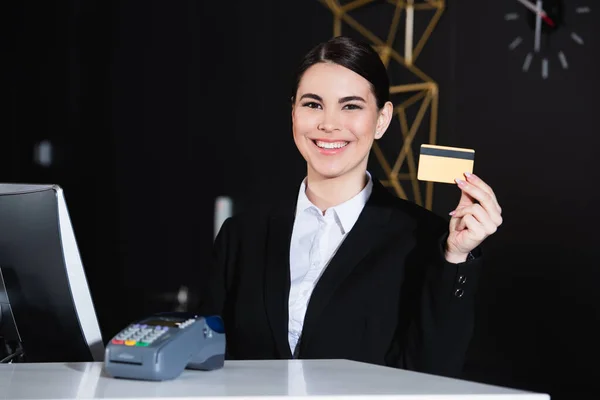 Administrador feliz segurando cartão de crédito perto do terminal de pagamento no hotel — Fotografia de Stock