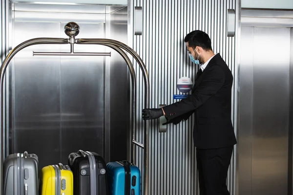 Fattorino in maschera medica in piedi con campanello vicino ascensore in hotel — Foto stock