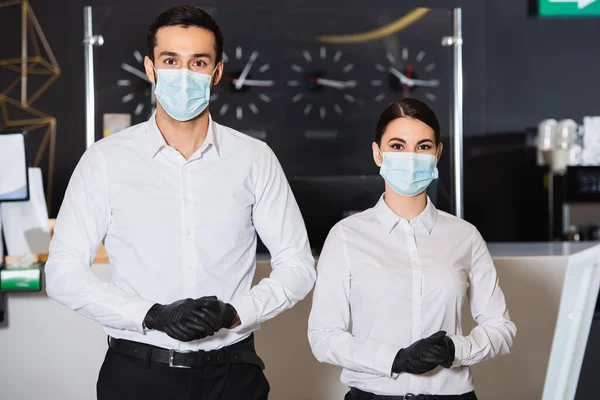 Recepcionistas en máscaras médicas y guantes de látex cerca de la recepción - foto de stock