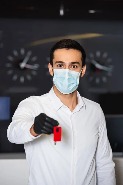 Recepcionista em máscara médica segurando chave de quarto desfocada — Fotografia de Stock