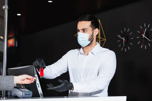 Administrator in latex gloves and medical mask giving room key to guest — Stock Photo