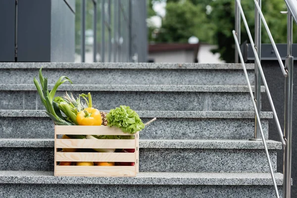 Box with fresh vegetables on stairs near building — Stock Photo