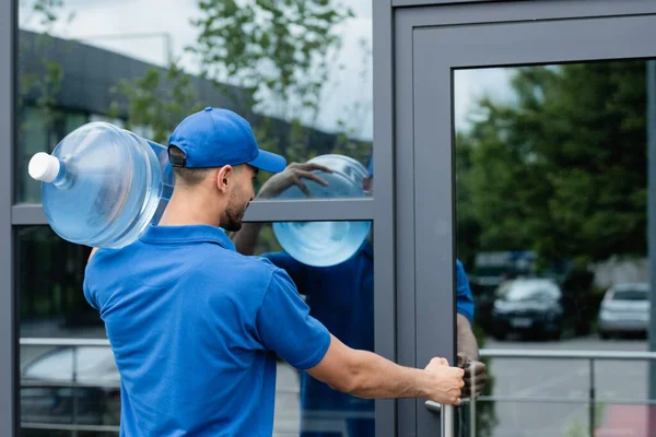 Muslim deliveryman holding bottle of water while opening door of building — Stock Photo
