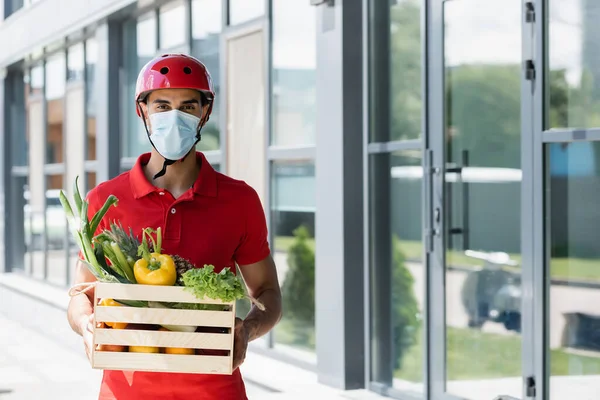 Muslim courier in helmet and medical mask holding fresh vegetables outdoors — Stock Photo