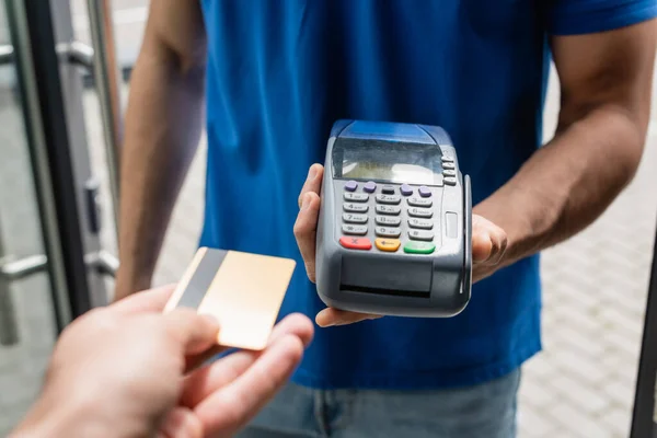 Vue recadrée de l'homme tenant la carte de crédit près du messager avec terminal de paiement — Photo de stock