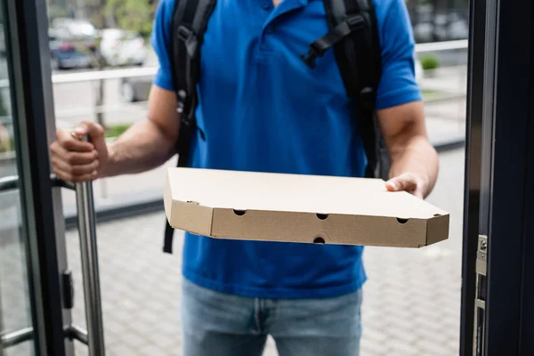 Cropped view of pizza box in hand of blurred courier near door — Stock Photo