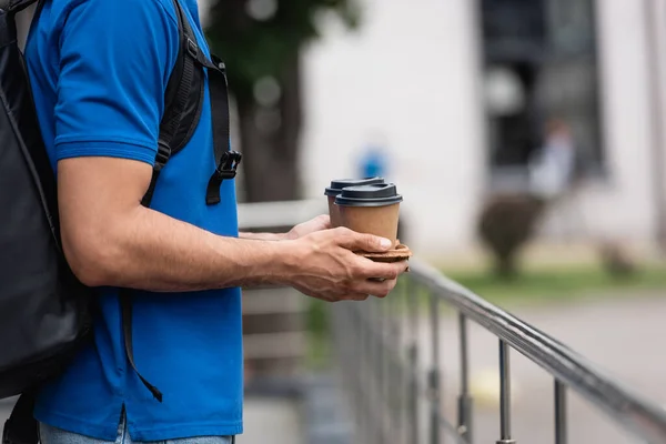 Cropped view of courier with backpack holding paper cups outdoors — Stock Photo
