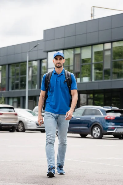 Arabian courier with backpack and smartphone walking on urban street — Stock Photo