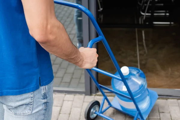 Cropped view of deliveryman holding cart with blurred bottle of water outdoors — Stock Photo