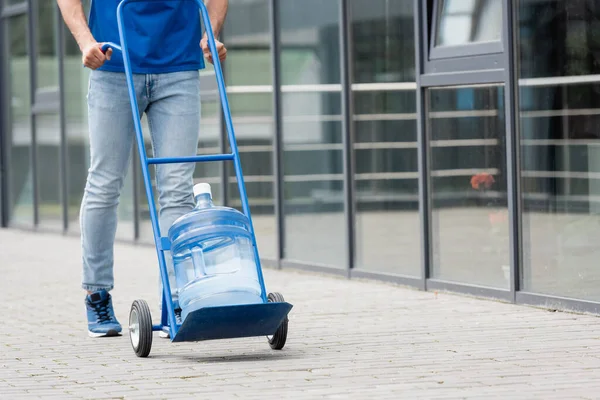 Cropped view of deliveryman pulling cart with bottle of water outdoors — Stock Photo