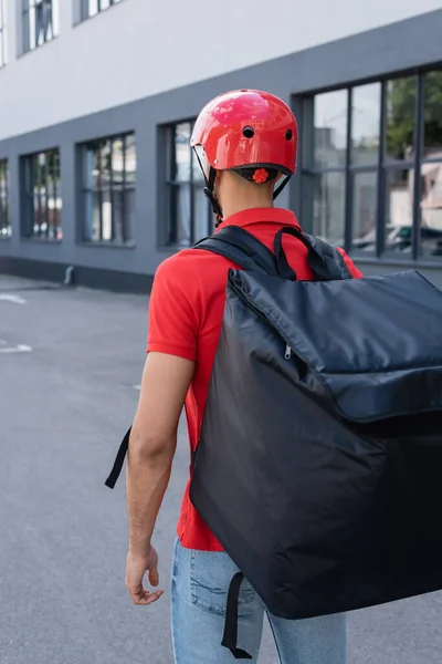 Back view of courier in helmet and thermo backpack standing outdoors — Stock Photo